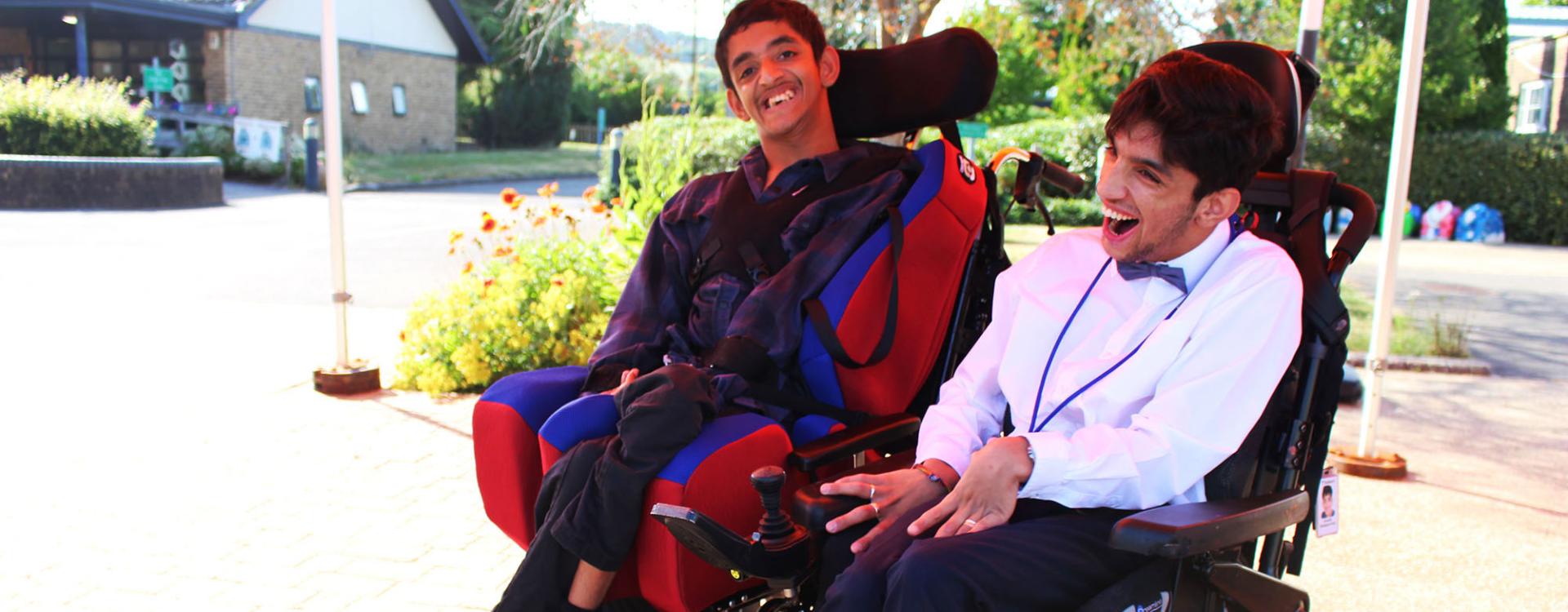 Two Treloar College student smiling and enjoying a sunny day outdoors near a building and garden. They are wearing a formal attire. 