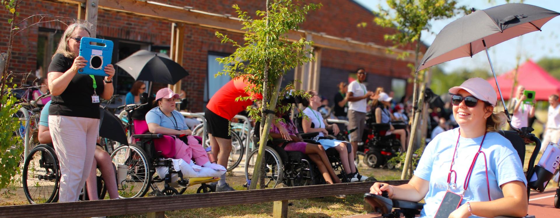 Treloar College staff and students enjoying an outdoor event on a sunny day with some holding umbrellas for shade.