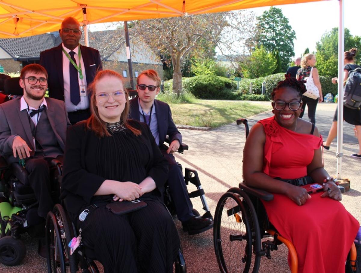 Group of 4 Treloar College students with a student support assistant gathered under an orange canopy outdoors on a sunny day during their prom.