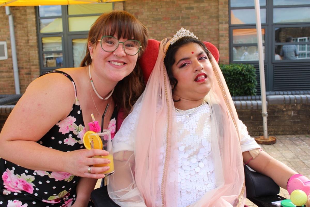 Treloar School student dressed up for her prom, posing for a picture with her student support assistant. The assistant is holding a decorated glass of orange juice.