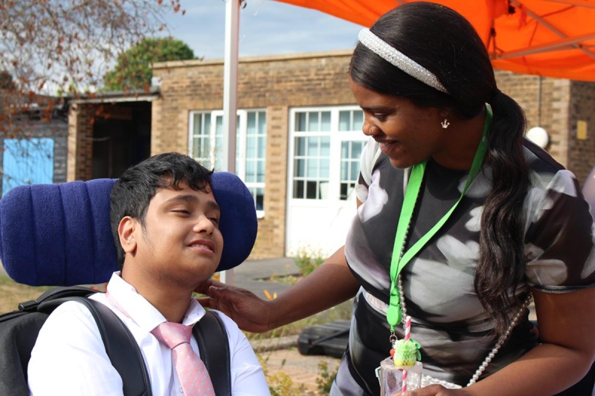 Treloar School student is smiling at his student support assistant; she put her hand on his shoulder while talking to him. He is wearing a white shirt with a pink tie.