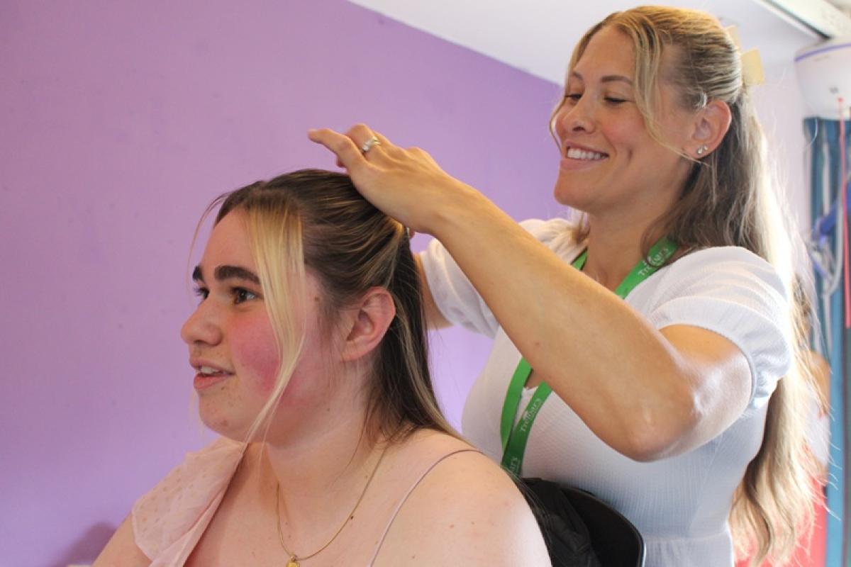 Treloar School student is having her hair done by her student support assistant. They are both smiling.