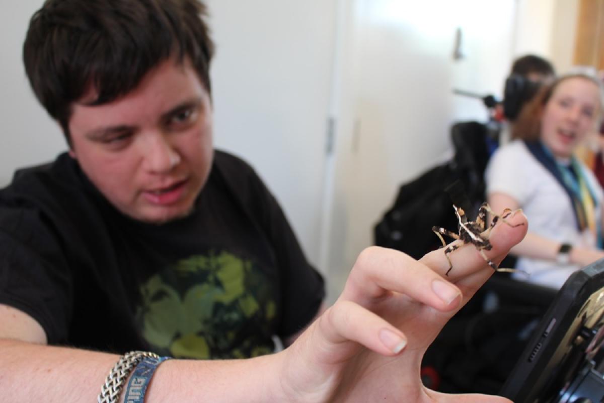There is  a small, camouflaged insect on Treloar College student's finger; other students blurred in the background.