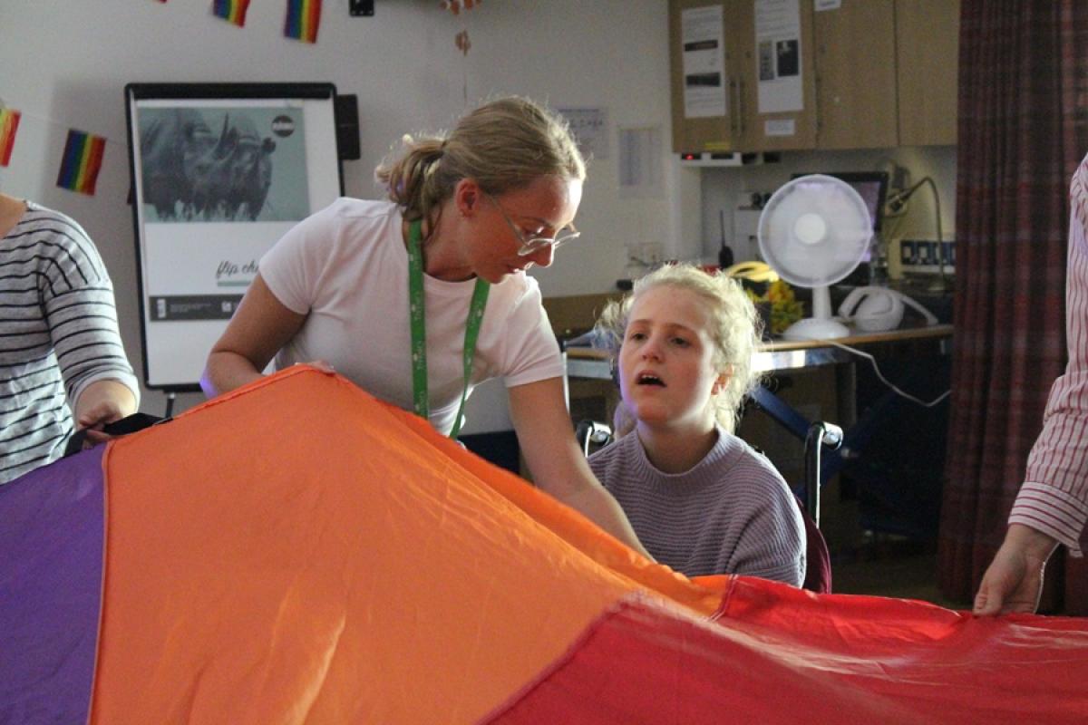 Treloar's student support assistant in a white shirt is helping Treloar College student hold onto a colorful parachute indoors.