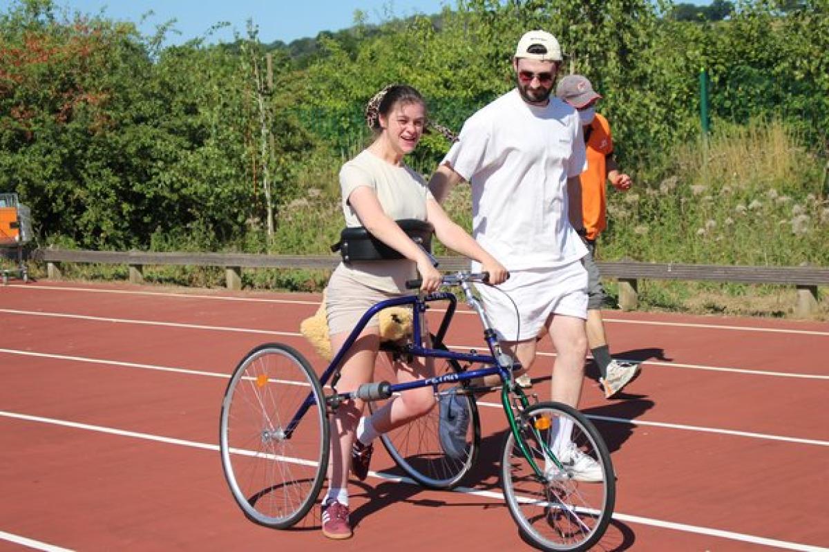 Treloar College student using a three-wheeled adaptive bike on a running track, assisted by her student support assistant who is walking beside her.