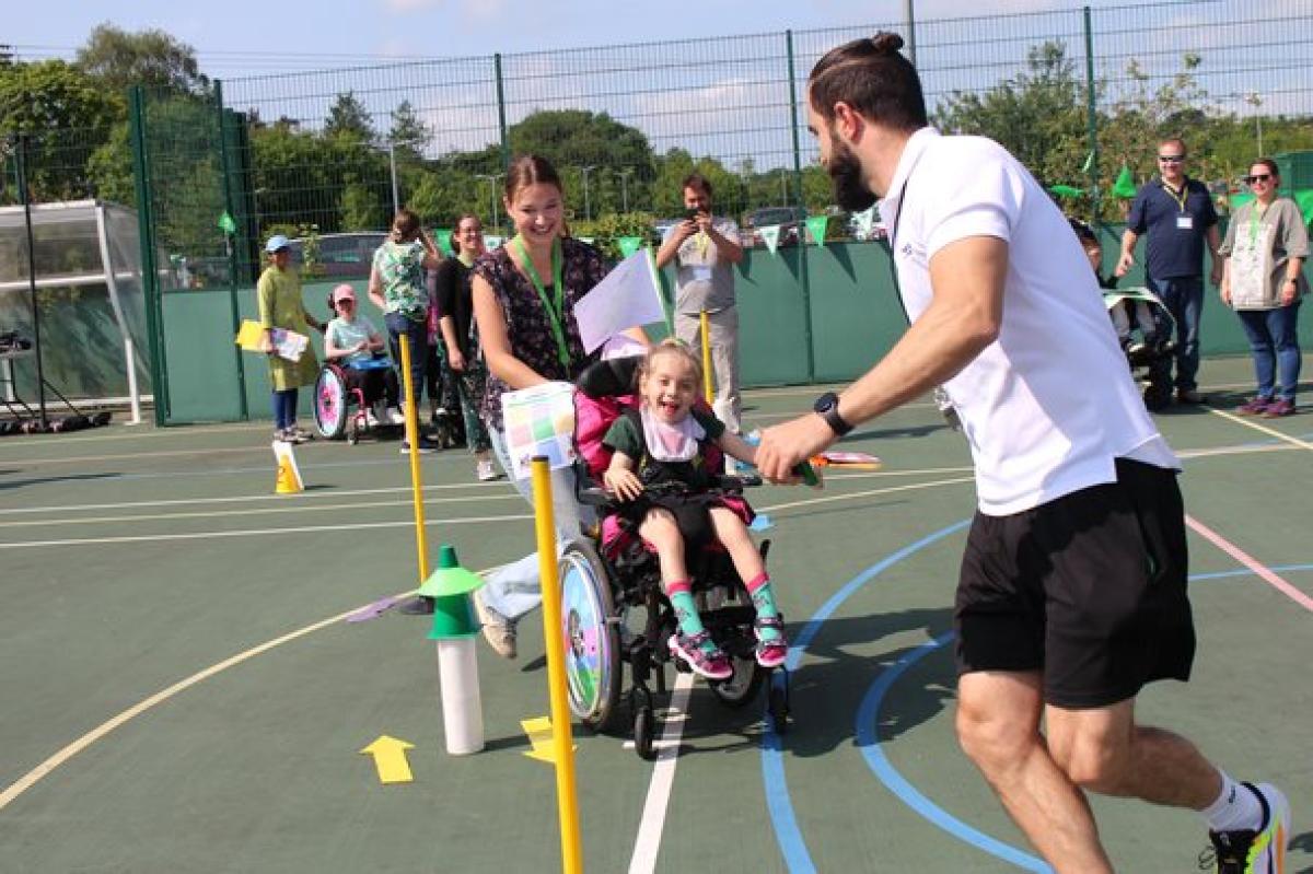 Treloar's primary student navigates an outdoor sports court obstacle course with assistance from 2 staff members.