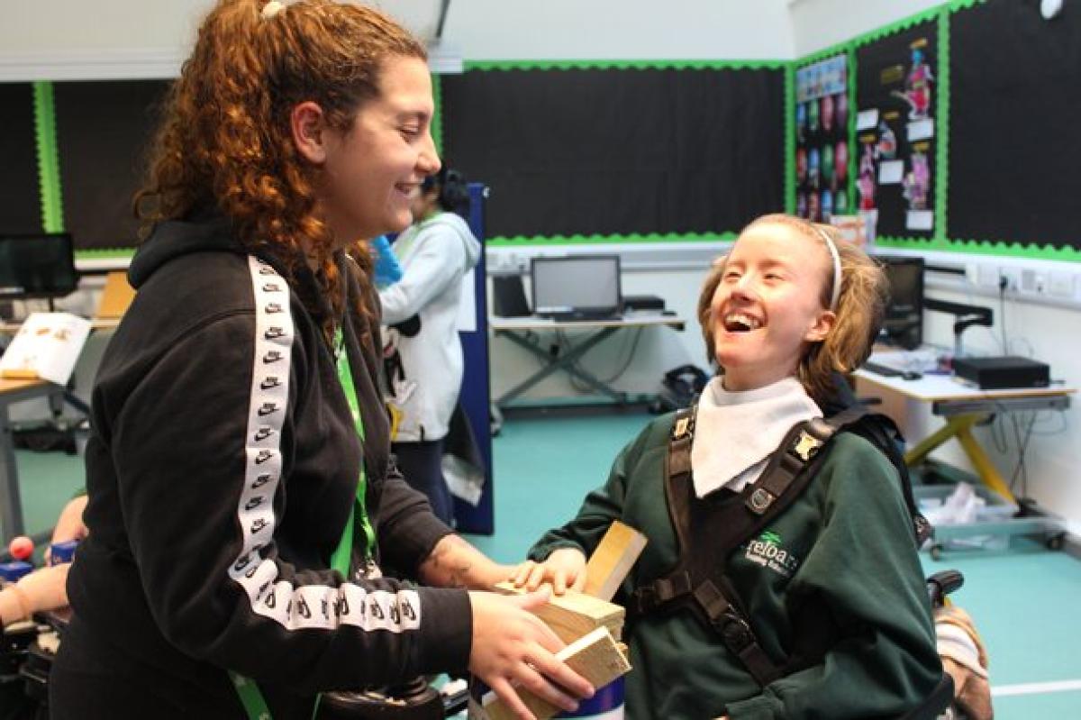 student smiling with support assistant, using bricks to balance