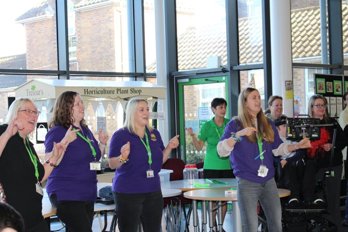 Group of Treloar's Makaton tutors participating in a Makaton celebration event. They are all singing and signing.