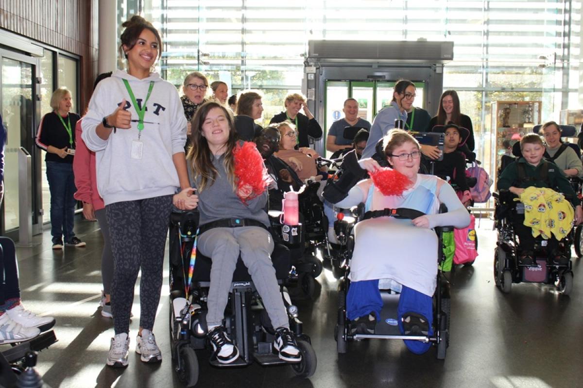 Treloar's students and staff participating in an indoor celebration event. Large windows in the background and some of the students are holding pom poms.