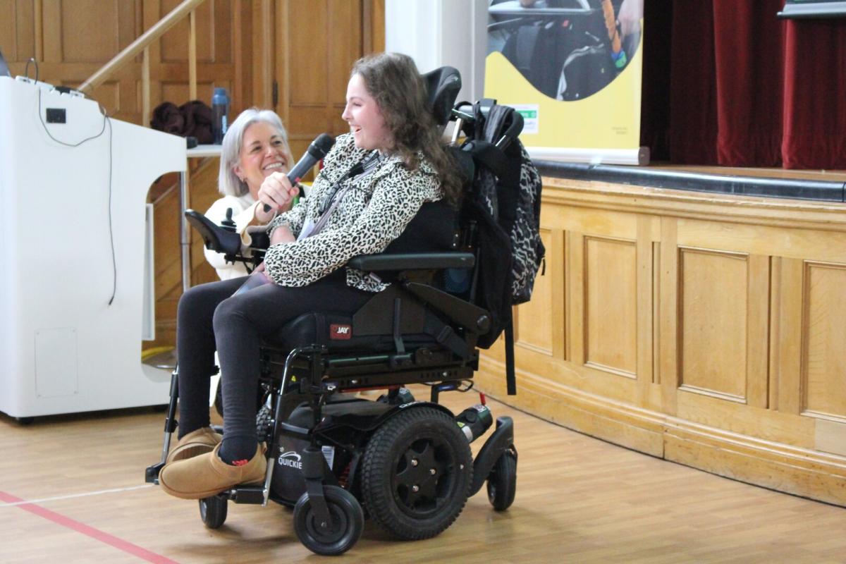 A Treloar College student is speaking into a microphone, to address a group of visitors, off camera