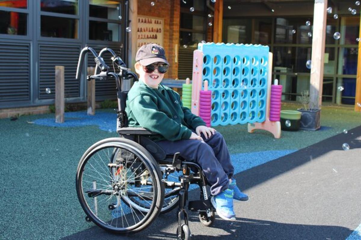 Treloar's primary student playing outdoors near a giant Connect Four game on a sunny day. Bubbles are in the air and the boy is happily posing for a photo.