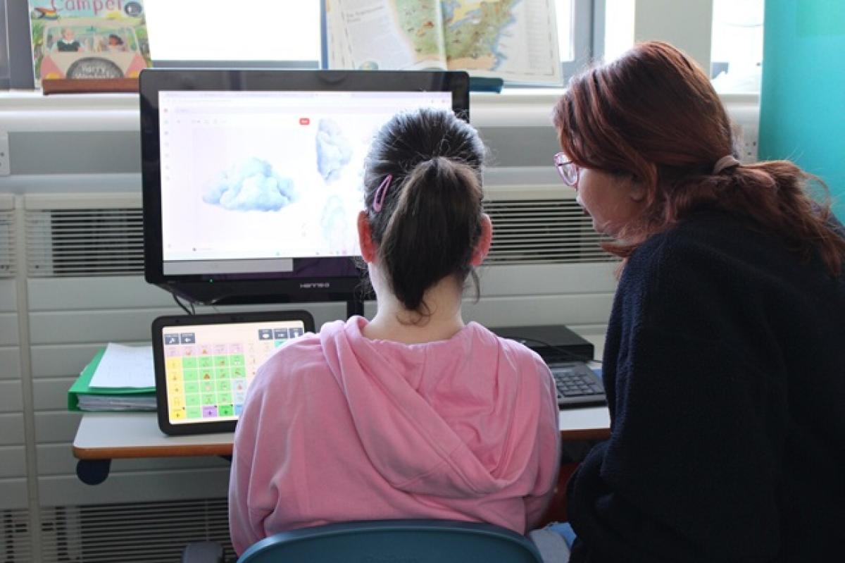 Treloar's student in a pink hoodie and her student support assistant with glasses looking at a computer screen displaying a cloud image in a classroom setting.