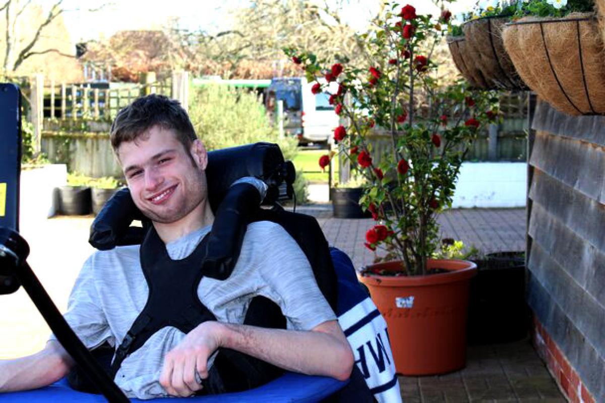 Treloar College student outdoors near a potted rose bush on a sunny day. He is smiling and posing for a photo.