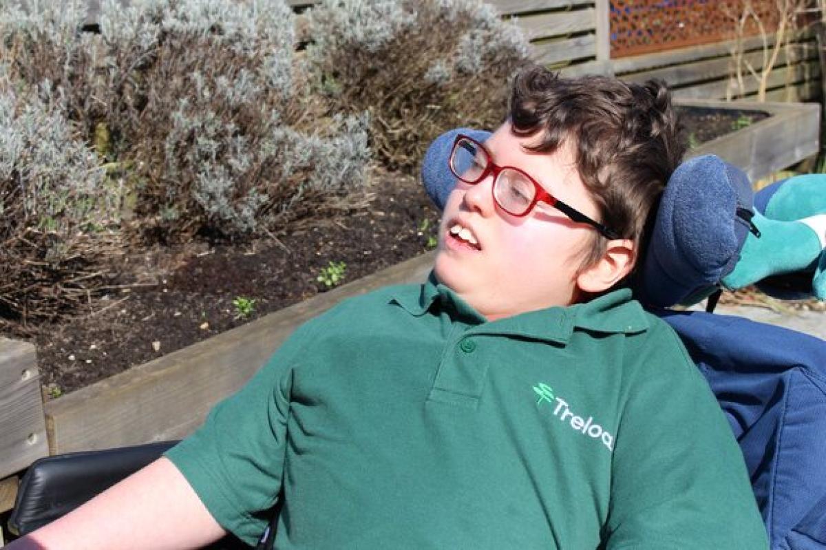 Treloar School student wearing a green Treloar's polo shirt outdoors in the sensory garden near garden beds with lavender shrubs.