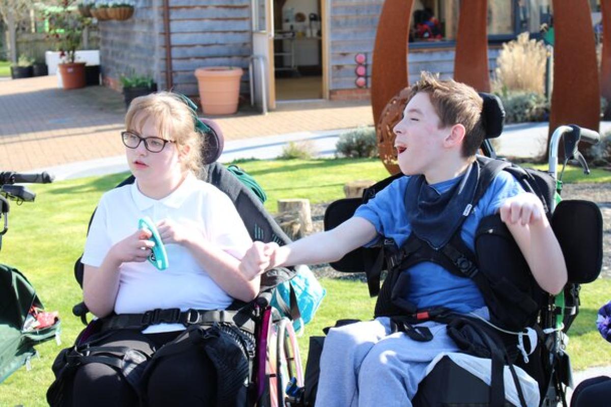 2 Treloar School students outdoors on a sunny day in the sensory garden. They are both listening to the teacher who is not in the picture.