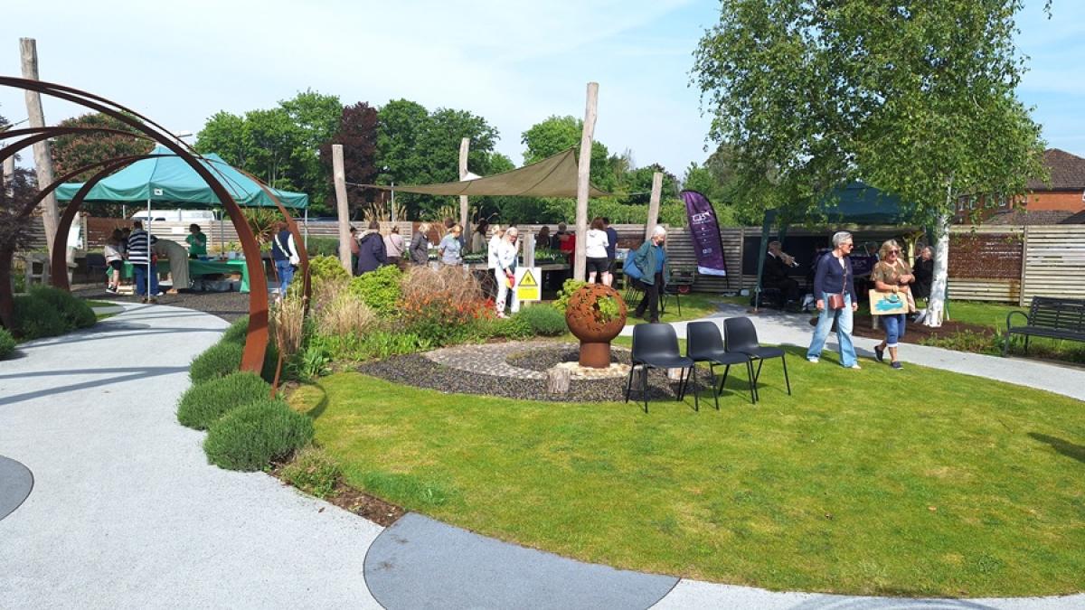 People gather at an outdoor garden event with tents and seating on a sunny day.