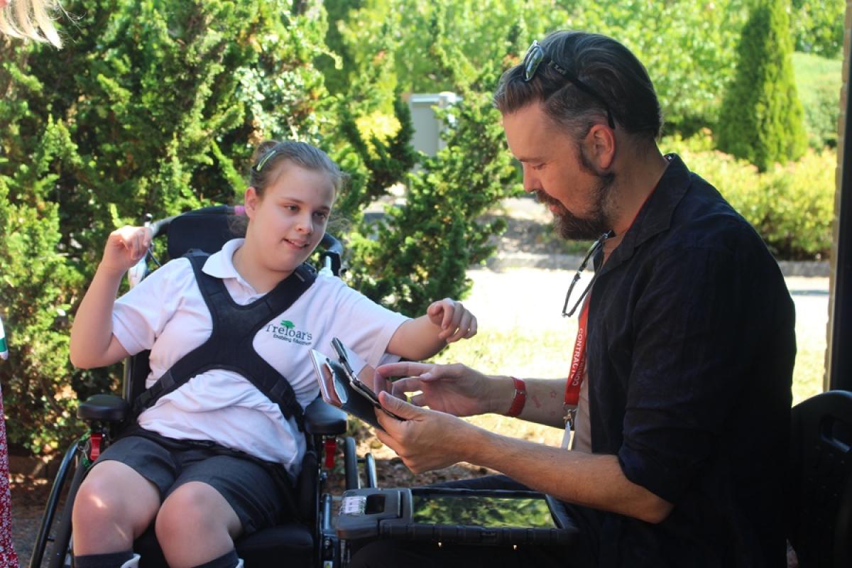 Treloar's student outdoors interacting with a man showing something on a smartphone under sunlight. She is wearing Treloar's summer uniform.
