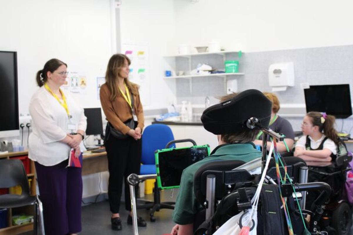 Two visitors stand in a classroom in front of Treloar's  students and staff. Everyone looks engaged and focused on what the visitors have to say.
