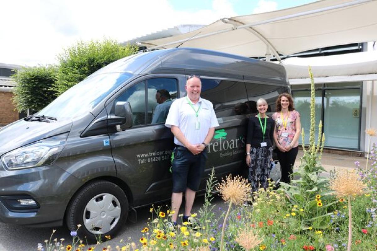 Three people stand beside a Treloar's minibus on a sunny day