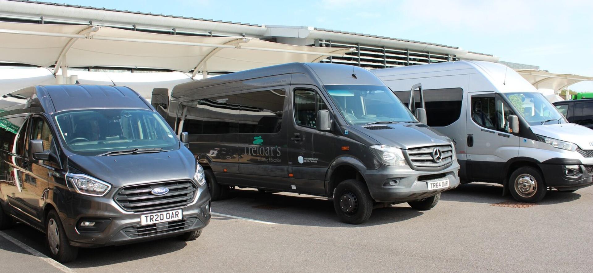 Three grey minibuses parked outside Treloar's reception area under blue skies