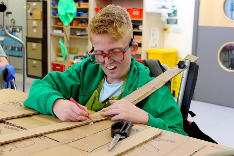 Treloar's student using a pencil to mark where to cut a long piece of cardboard; he is very focused on the task.