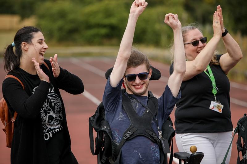 Treloar College student cheering on, raising his both arms up in the air - his 2 assistants are walking next to him and clapping. Everyone is having fun.