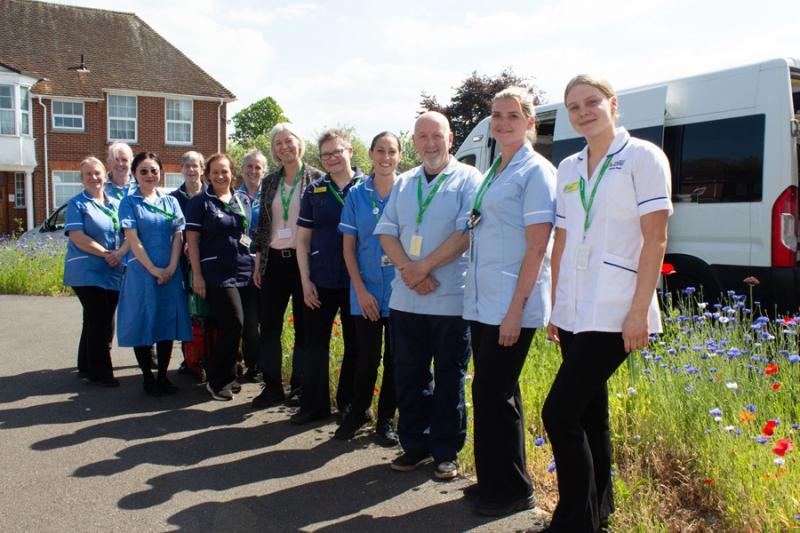 Treloar’s Nursing and Healthcare Team lined up outdoors posing for a group photo. It's a sunny day and behind them, there is a row of wild blue and red flowers.