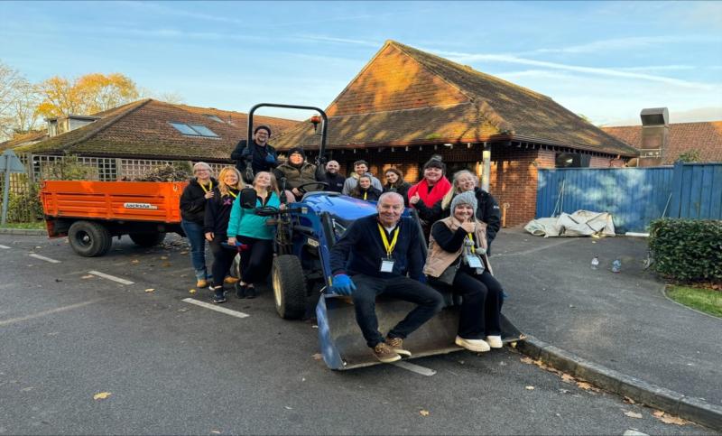 A group of volunteers gathered around a tractor, some of them sitting on it, some leaning against it. All looking at the camera and smiling.