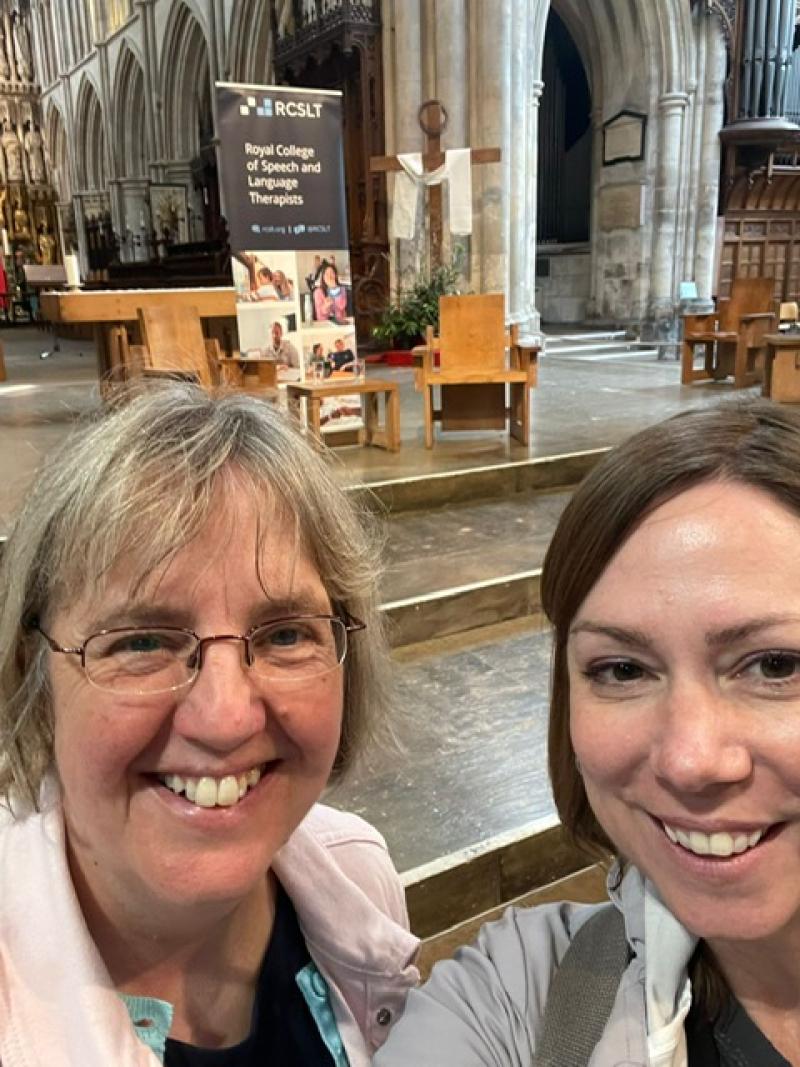 A selfie taken by 2 Treloar's Speech and Language Therapists, Emily Ball and Caroline Weighton, at a special non-denominational Anniversary event at Southwark Cathedral. A banner of the event in the background. Emily and Caroline are smiling to the camera.