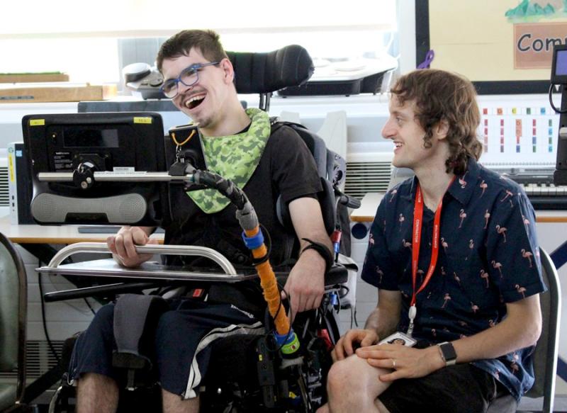 Oliver Squibb, Clarion Peripatetic Teacher during a music workshop, sitting next to Treloar's student who is using Clarion - both are happy and are smiling.