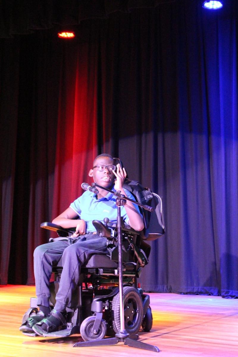 Treloar College student on the stage during Treloar's Got Talent competition. The stage is lit up with colourful lights. The student is singing and is very focused on his performance.