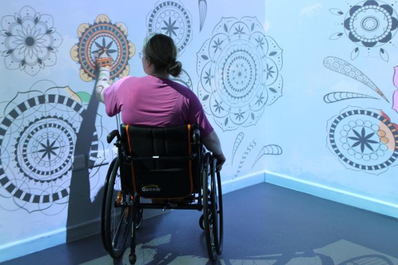 Treloar College student wearing a pink shirt and is interacting with intricate black and white mandala designs projected on the wall.