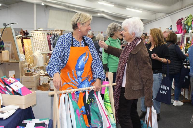 A stall holder at the Dummer Fair wearing a bring orange apron and talking to a customer in front of her stall.