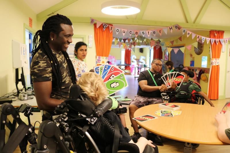 students and 2 staff play uno with extra large cards. They are smiling and seated around a large round table