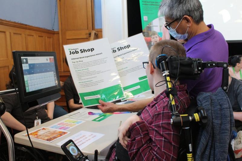 Treloar College student, wearing glasses and reading a Job Shop informational flyers held by a Treloar's staff member in a purple shirt at a table with documents.