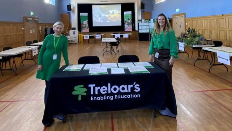 Karen Florence and Mary Menzies, Treloar's Employability Coordinators stand behind a Treloar's Enabling Education information table in a large hall with wooden panelling and multiple labelled tables.