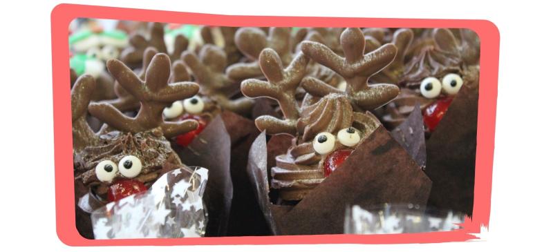 A tray of chocolate cupcakes with swirling chocolate frosting, gummy eyes, cherry nose and antlers to look like reindeer