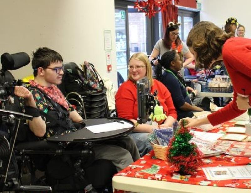 Treloar College student at a stall with his assistant at the Christmas Fair; they are selling Christmas decorations.