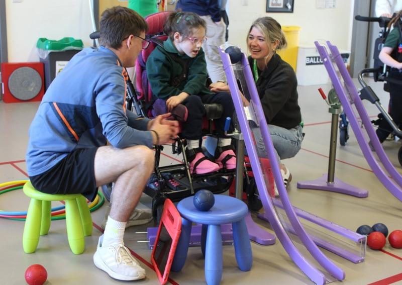 Treloar's primary student playing boccia with a college student from a local college assisting her and observing her use a ramp.