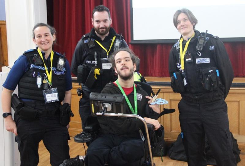 3 police officers with Treloar's student pose together inside a hall with red curtains and a wooden stage behind them.