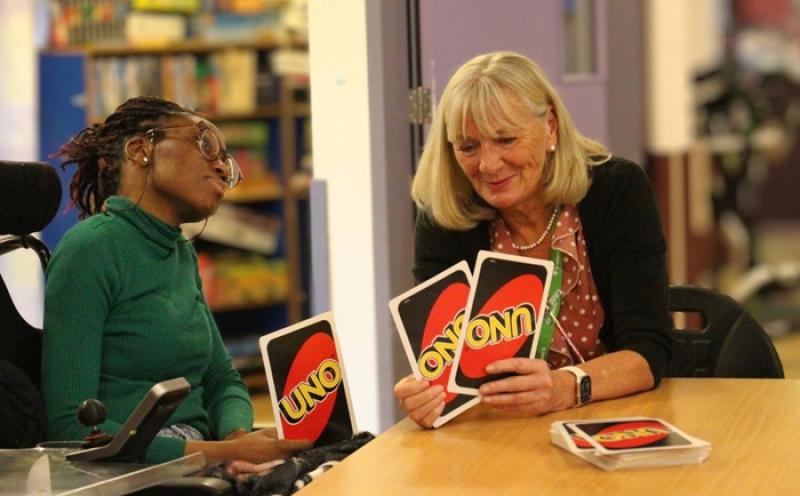 Treloar's student and a residential manager sitting at a table playing UNO card game, with the student holding cards and the manager showing a single card.