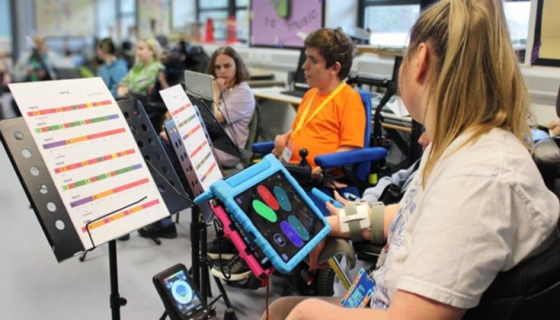Treloar's student using a tablet to play the clarion in a classroom setting with music sheets on stands nearby.