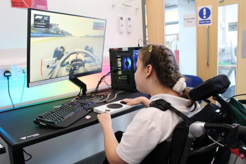 Treloar's student playing a racing video game on a desktop computer with a large monitor in a bright room.
