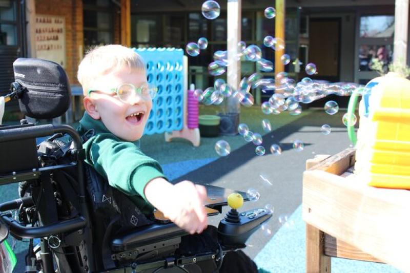 Treloar's primary student joyfully reaching out to catch floating soap bubbles outdoors on a sunny day.