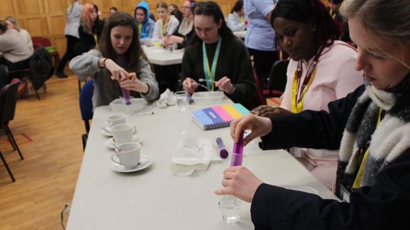 Group of first-year nurses around a table engaging in a hands-on activity with test tubes and notebooks in a classroom setting.