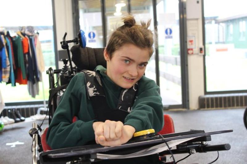Treloar School using head switches and a hand switch to drive her wheelchair in a bright indoor space.