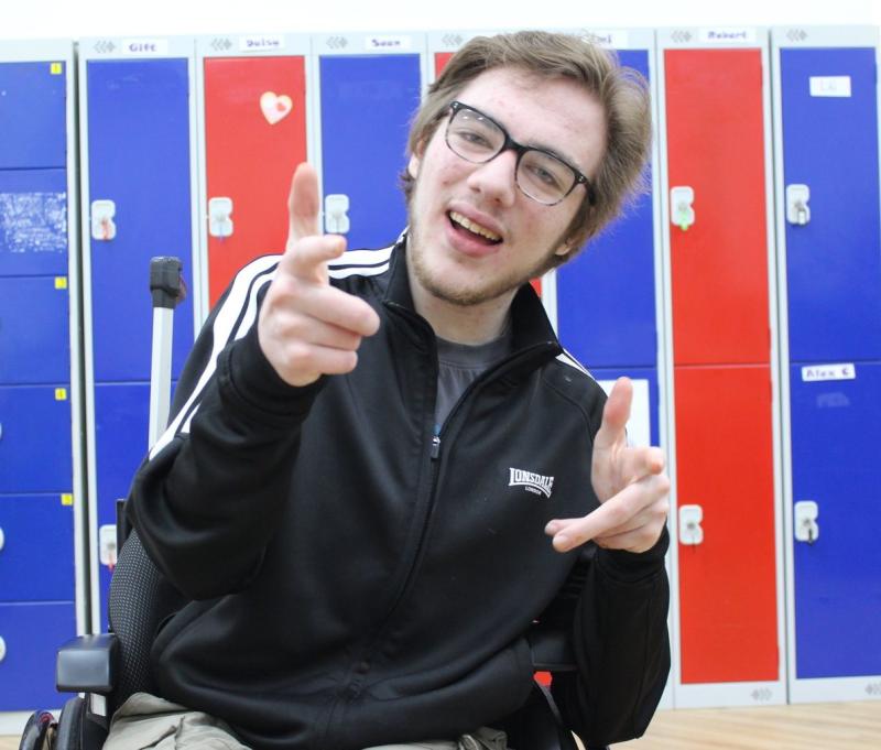 College student wearing a black zip-up top sitting in wheelchair, in front of red and blue lockers