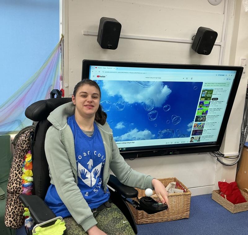 Treloar College student in front of a large screen displaying a YouTube video of bubbles against a blue sky.