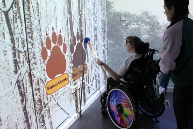 Treloar's student interacting with a large touchscreen displaying bear paw prints and options like 'Repeat Chapter' and 'Next'.