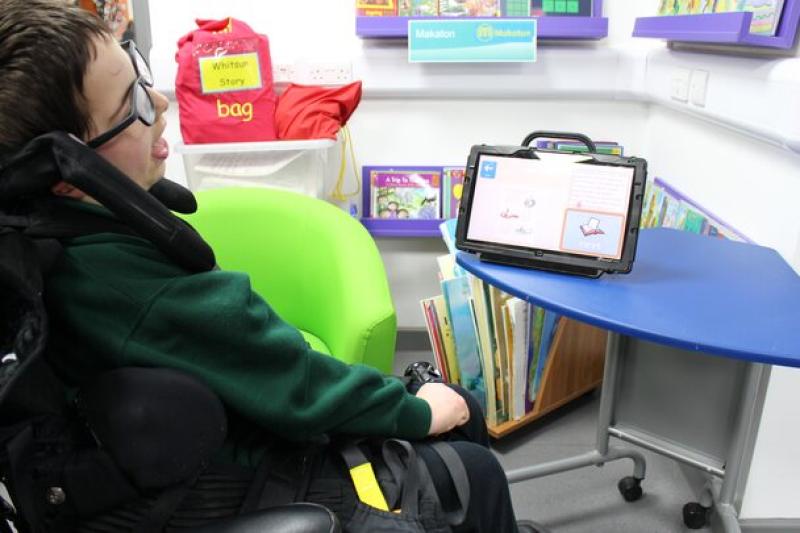 Treloar's primary student using a tablet on a blue table in a colourful classroom corner with books and educational materials.